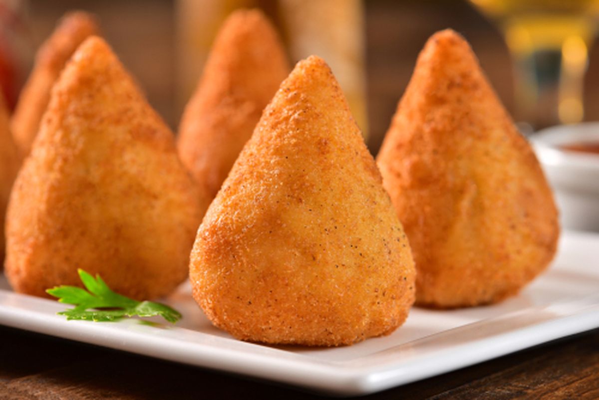 Coxinha com Massa de Batata 1 Prato com coxinhas douradas e crocantes, com recheio de frango visível na ponta, servidas com molho de limão e pimenta