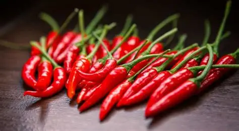 Pimenta-de-cheiro (Malagueta): O Fogo Aromático da Cozinha Brasileira 1 Pimentas malaguetas vermelhas e brilhantes em um prato de cerâmica, com folhas verdes ao fundo