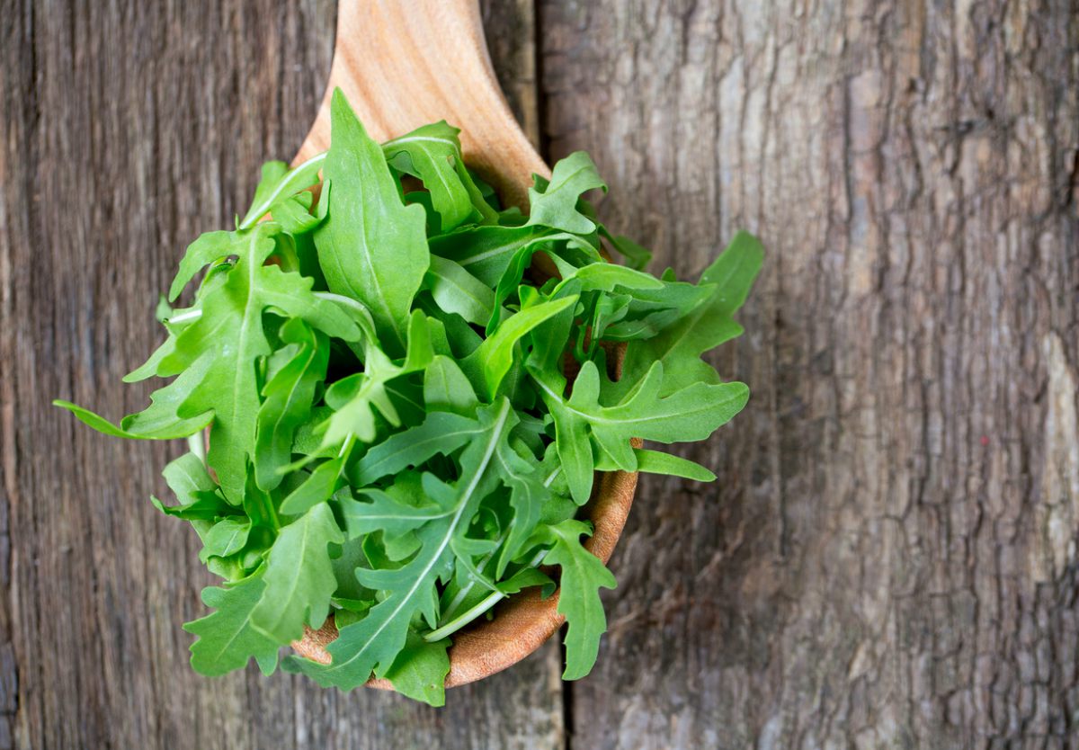 Rúcula: O Verde Aromático que Eleva Qualquer Prato 1 Maço de rúcula fresca sobre tábua de madeira, folhas verdes escuras e crocantes